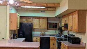 A compact kitchen with wooden cabinets, a central island, a ceiling fan, and a black trash bin. - Inviting & Spacious! Unique indoor and outdoor vibe! (Walsenburg)