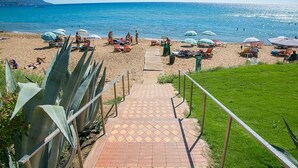 Ein Strand mit einem gepflasterten Weg zum Wasser, umgeben von Sonnenschirmen und Liegestühlen.
