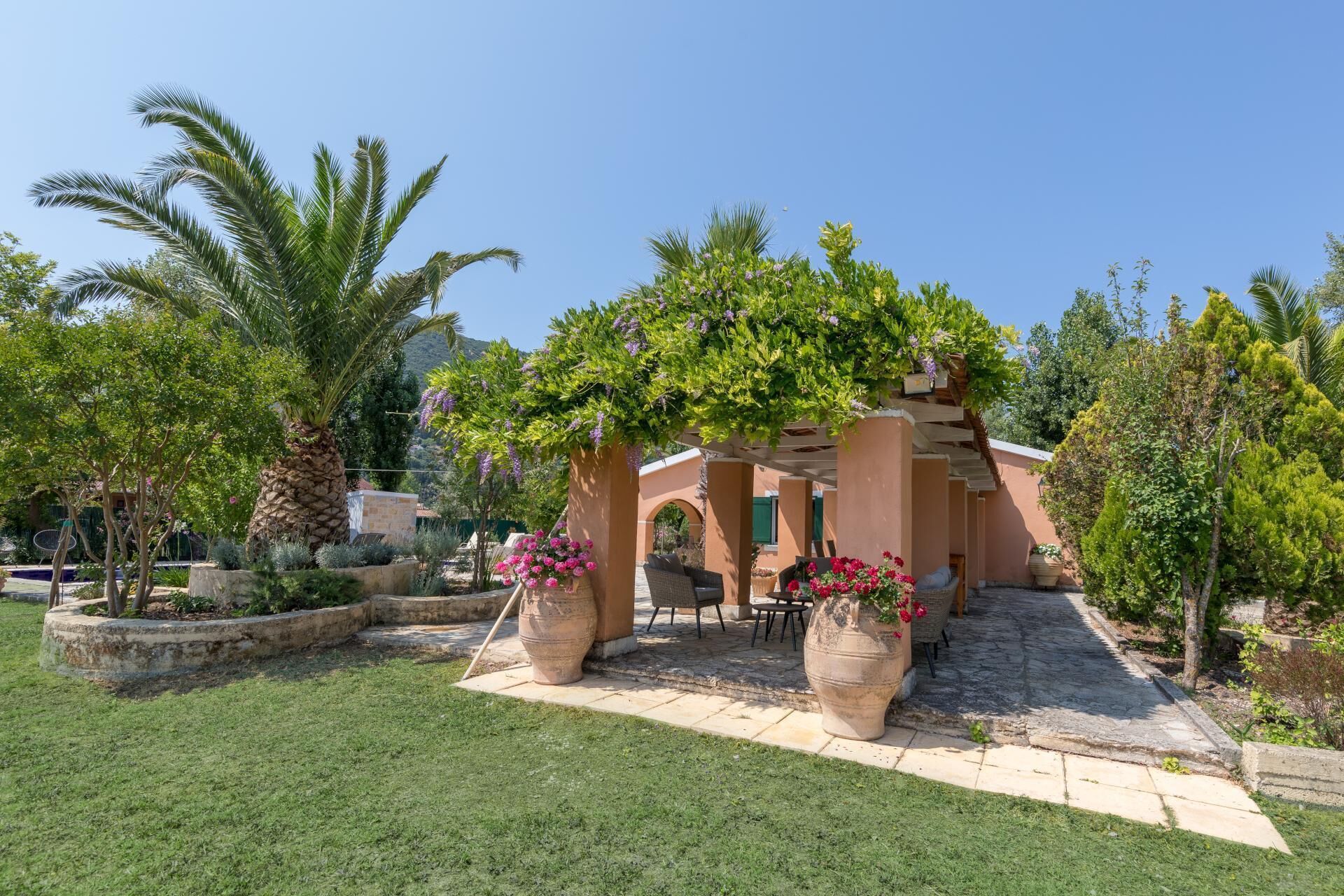 A covered outdoor seating area with a pergola, potted plants, and a stone pathway.