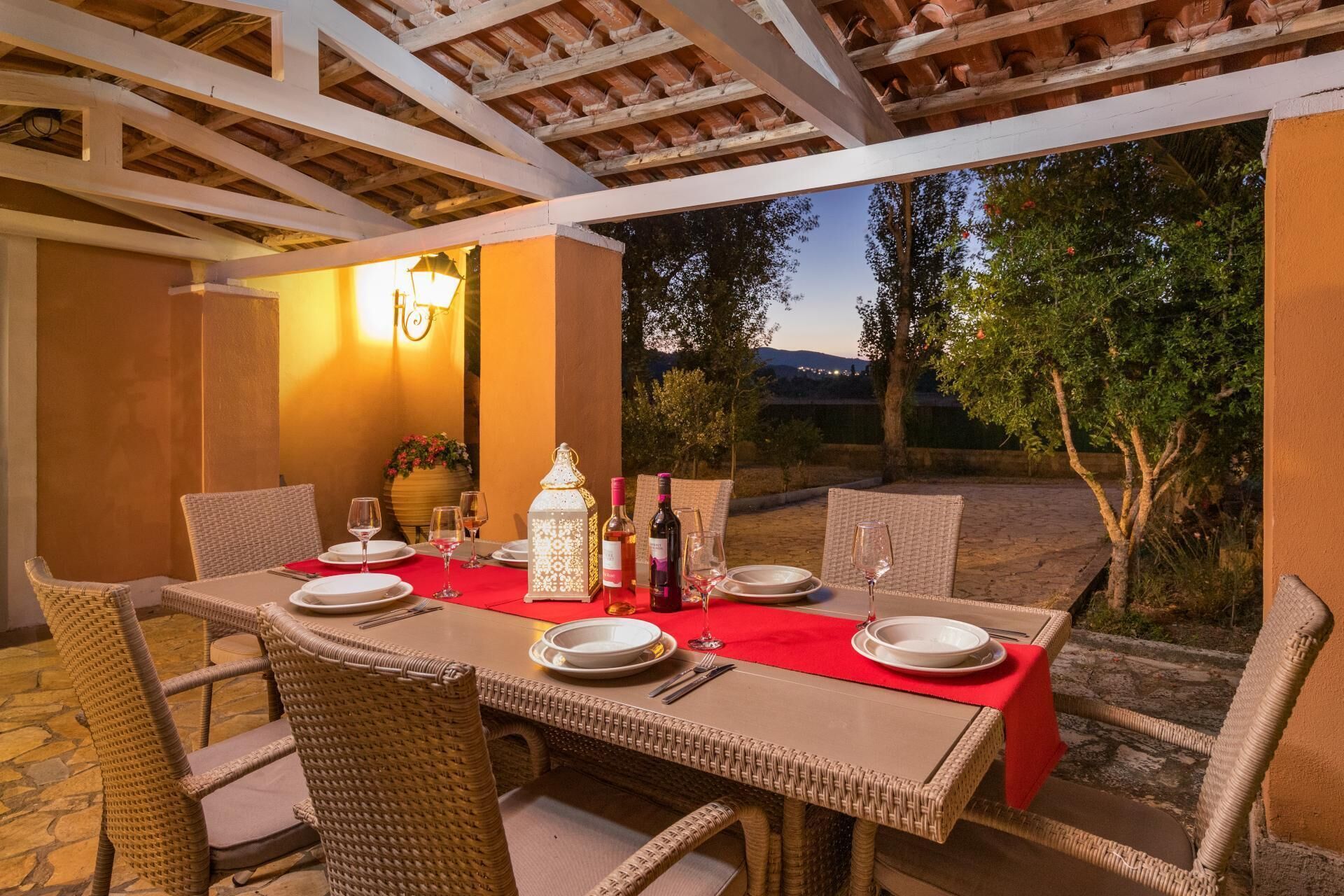 An outdoor dining area with wicker chairs and a table set for two, featuring wine bottles and glasses.