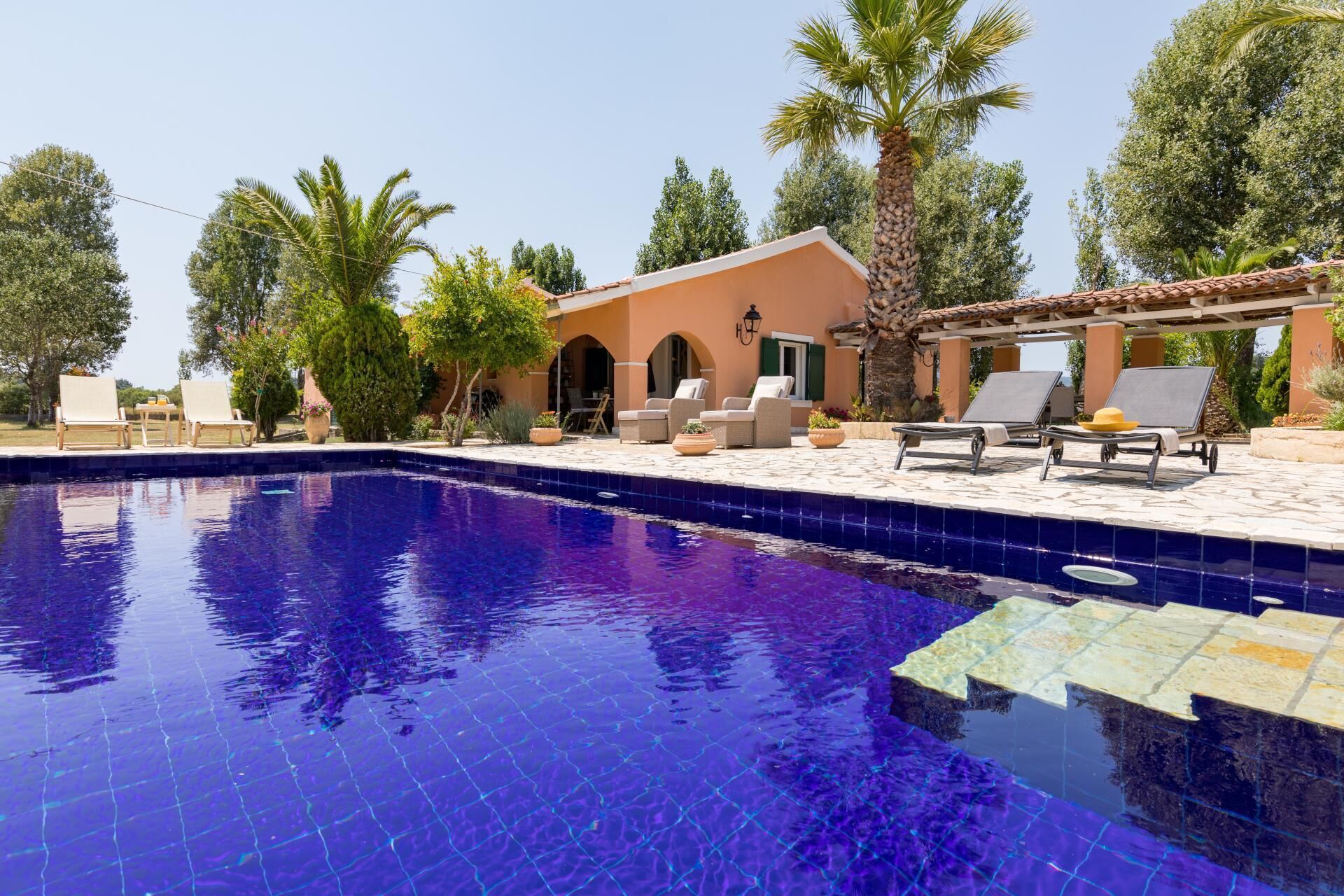 Une piscine avec des chaises longues et un bâtiment doté d’arches et d’un toit en tuiles.