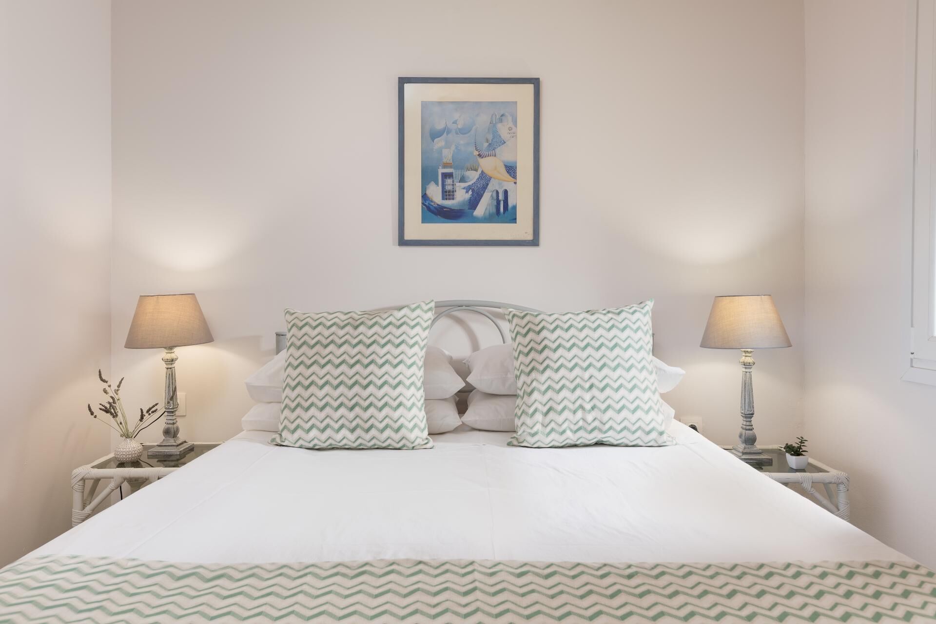 Un letto rifatto con due cuscini, un quadro incorniciato sopra e due comodini con lampade.