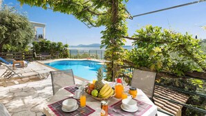A poolside breakfast setup with a table, chairs, and a view of the pool and mountains. - Appealing 2 Bedroom Villa, A/C, Private Pool, Panoramic Sea Views - In Nissaki, just 450m to Beach! (Nissaki)