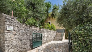 A stone pathway leading to Villa Klima, surrounded by lush greenery and a stone wall. - Appealing 2 Bedroom Villa, A/C, Private Pool, Panoramic Sea Views - In Nissaki, just 450m to Beach! (Nissaki)