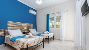 A room with two beds, a TV, and a window with curtains. - Appealing 2 Bedroom Villa, A/C, Private Pool, Panoramic Sea Views - In Nissaki, just 450m to Beach! (Nissaki)