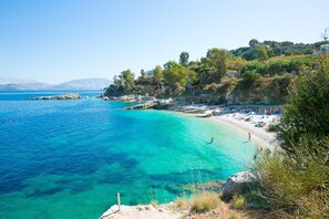 A coastal beach with clear turquoise waters, rocky outcrops, and a few people enjoying the sun.