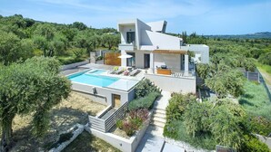 Una casa moderna de dos pisos con piscina, mobiliario exterior y vista a la vegetación circundante.