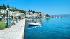 Un pueblo costero con un paseo marítimo adoquinado, barcos amarrados a la orilla y edificios con balcones.