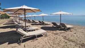 En strand med rader av solstolar och parasoller, en klar himmel och ett lugnt hav.