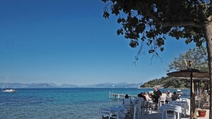 En restaurang vid havet med uteservering och utsikt över vattnet, en brygga med båtar och fri sikt över kustlinjen.