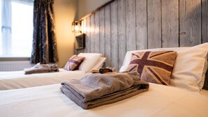 A hotel room with two beds, each with a pillow featuring a Union Jack design, a folded blanket, and a bottle. - York Lodge Pet Friendly (East Sussex)