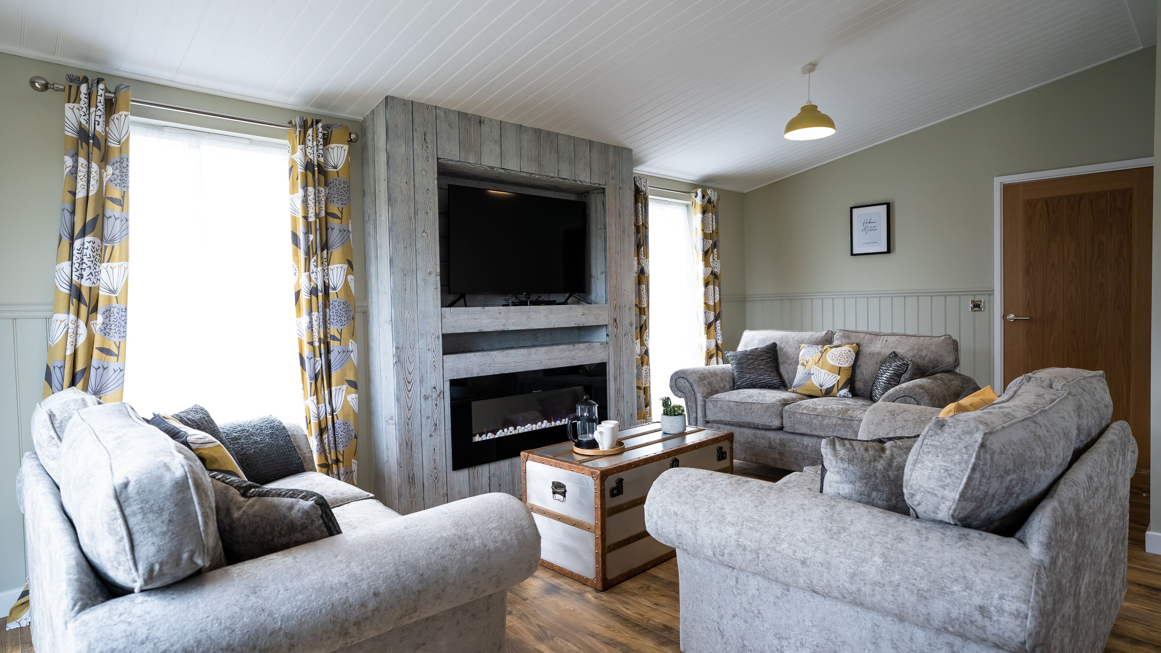 A living room with a fireplace, two grey sofas, a coffee table, and patterned curtains.