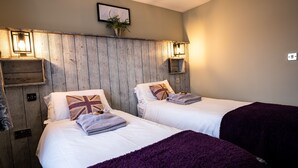 A room with two beds, wooden paneling on the wall, a framed picture, and a small shelf with a plant. - York Lodge Pet Friendly (East Sussex)