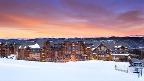 Eine große Lodge mit mehreren Gebäuden, einer Skipiste im Vordergrund und Bergen im Hintergrund.