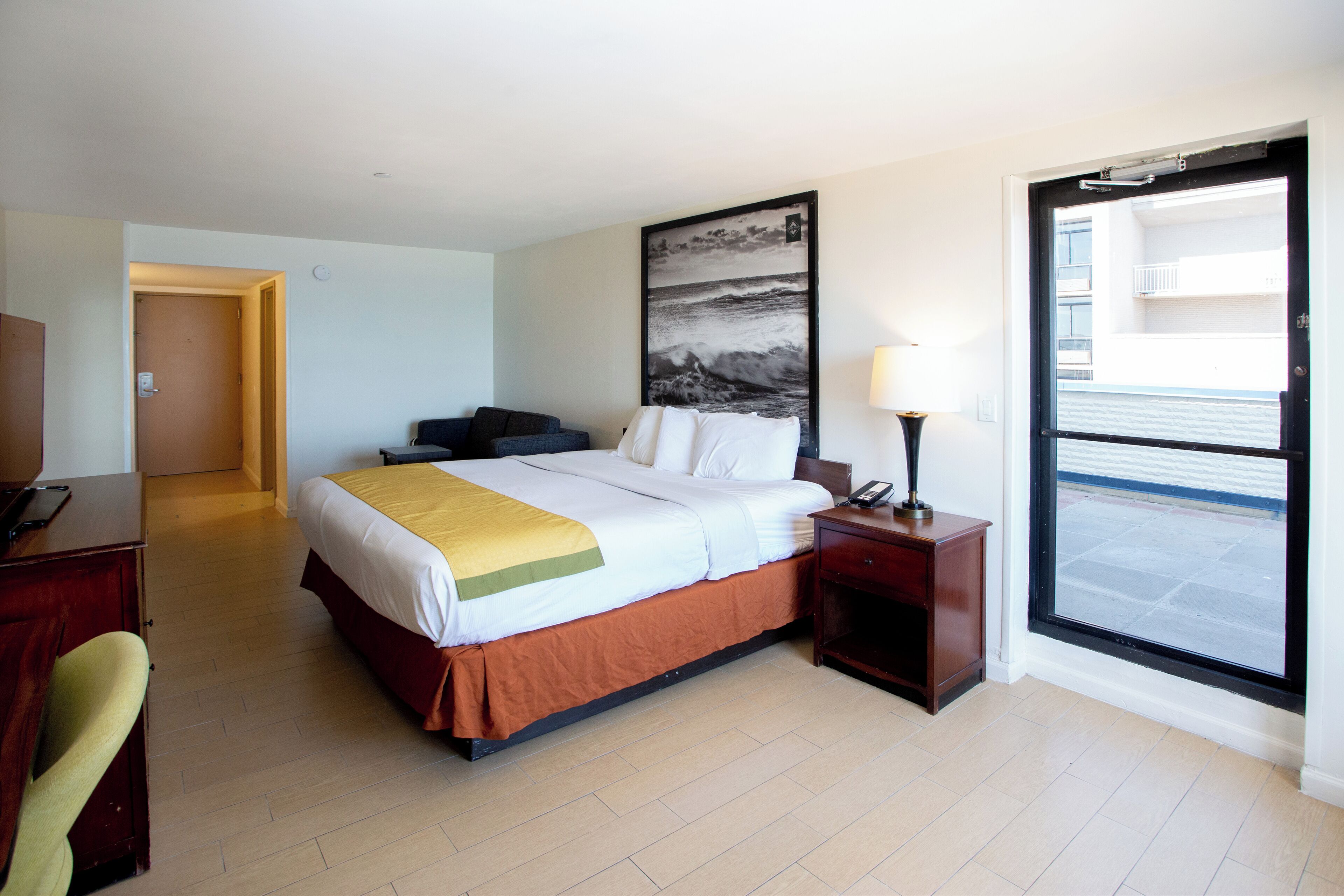 Ein Hotelzimmer mit Bett, Schreibtisch, Stuhl, Nachttisch, Lampe und einem großen Fenster mit Meerblick.