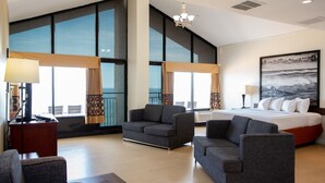 Una habitación de hotel moderna con una cama grande, dos sillones, una mesita y un ventanal con vistas a la ciudad.