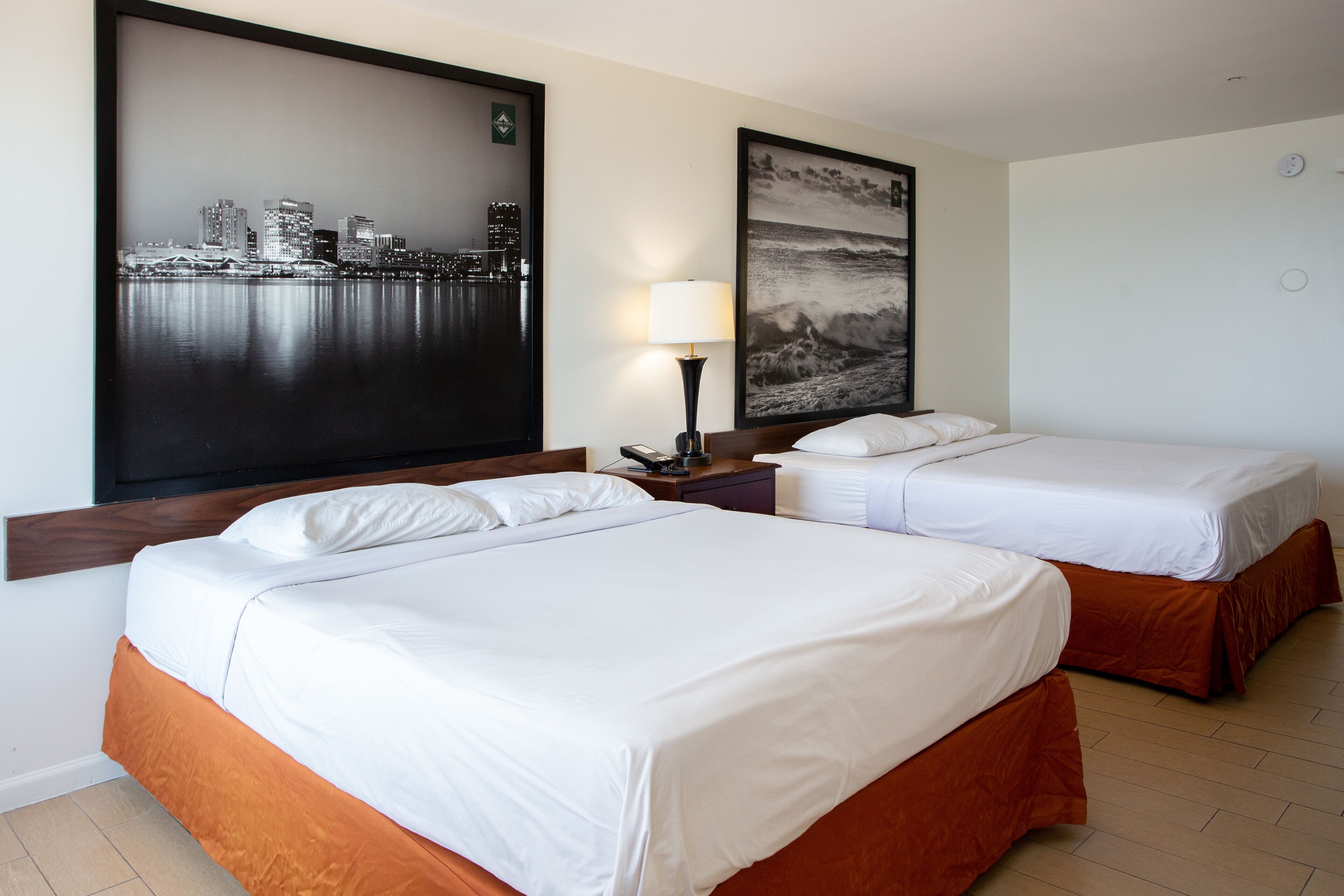Una habitación de hotel con dos camas, un cuadro de un paisaje urbano, una lámpara y un reloj en la pared.