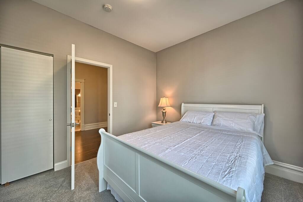 Un dormitorio con una cama, una mesita de noche, una lámpara y una puerta que da a otra habitación.
