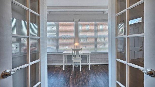 A room with a table and chair, large windows with blinds, and a view of buildings outside. - Suites on Seneca - Lovely 2 Bed/1 Bath Apartment (Harrisburg)