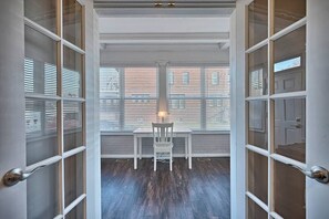 A room with a table and chair, large windows with blinds, and a view of buildings outside.
