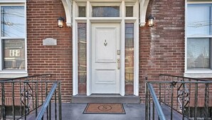 A brick building with a white front door, two windows on either side, and a metal gate in front. - Suites on Seneca - Lovely 2 Bed/1 Bath Apartment (Harrisburg)