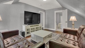 A living room with a flat-screen TV, leather sofas, a coffee table, and a lamp.
