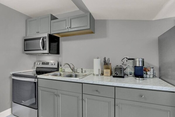 Une cuisine moderne avec des meubles gris, un four à micro-ondes encastré, une cuisinière et une machine à café.