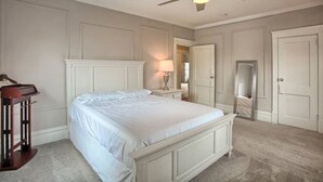 Un dormitorio con una cama blanca, un ventilador de techo, una mesita de noche con lámpara y un aparador.