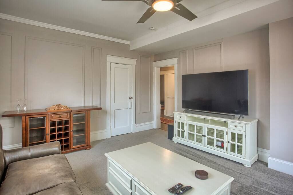 A living room with a flat-screen TV on a white cabinet, a leather couch, and a ceiling fan.