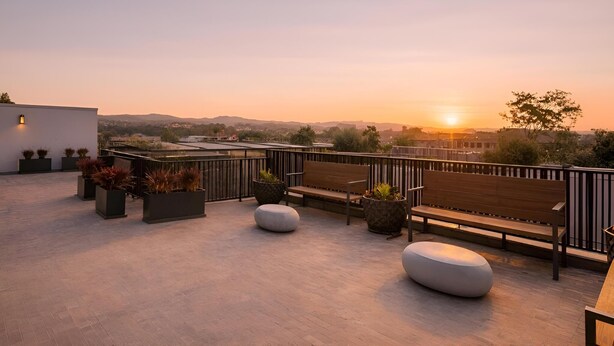 A rooftop terrace with seating, planters, and a view of the sunset.
