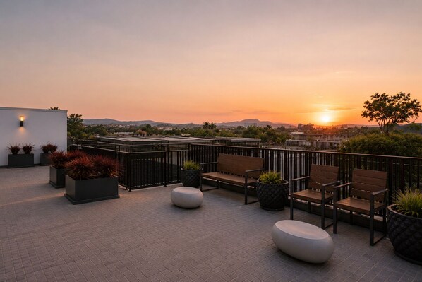 Une terrasse sur le toit, aménagée avec des sièges, des jardinières et offrant une vue sur le coucher de soleil.