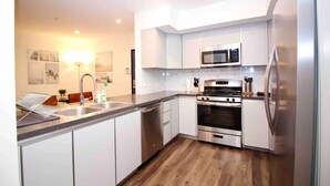 A modern kitchen with white cabinets, stainless steel appliances, and a wooden floor.