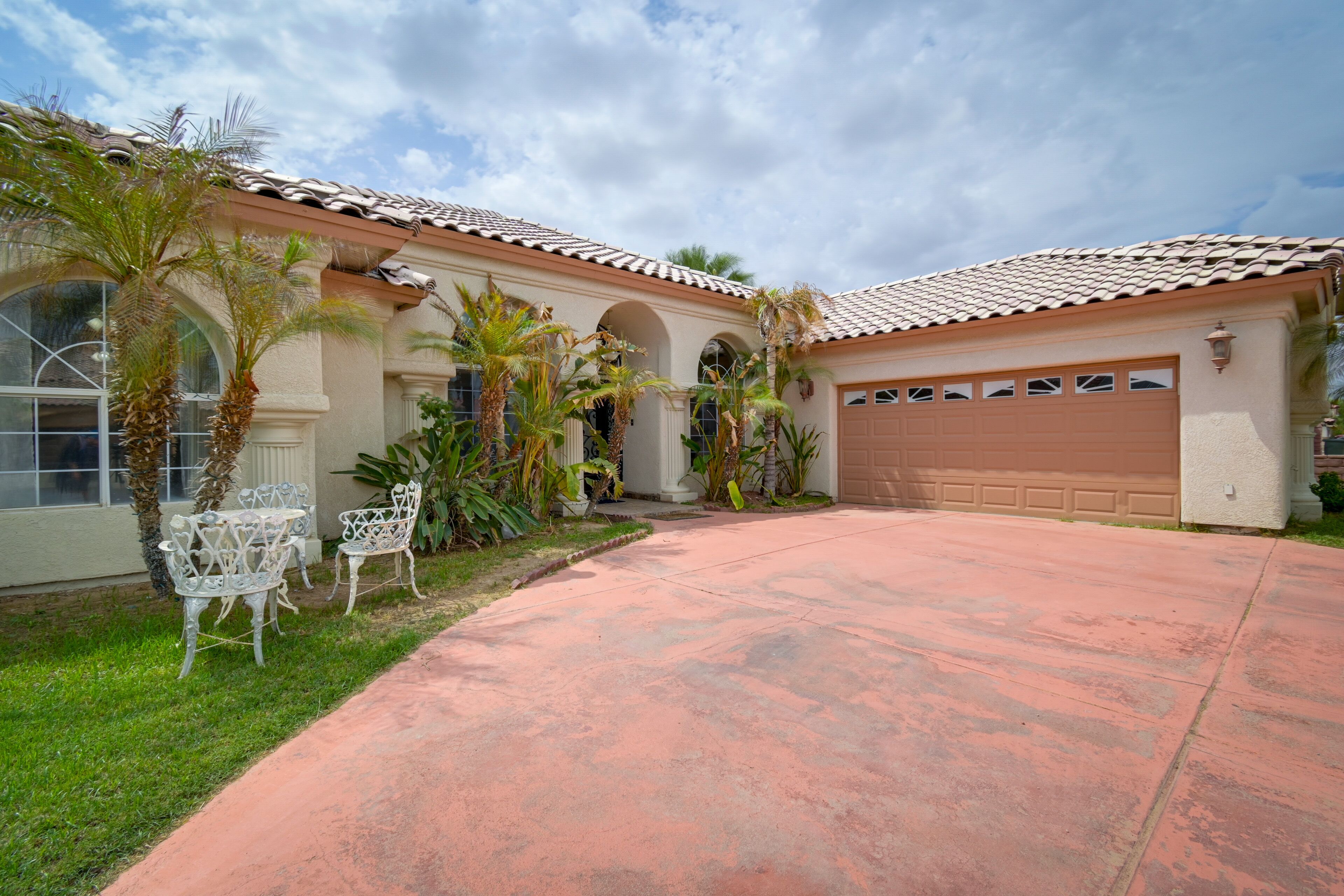 Uma propriedade residencial com entrada por automóvel, garagem e área externa para sentar com cadeiras.