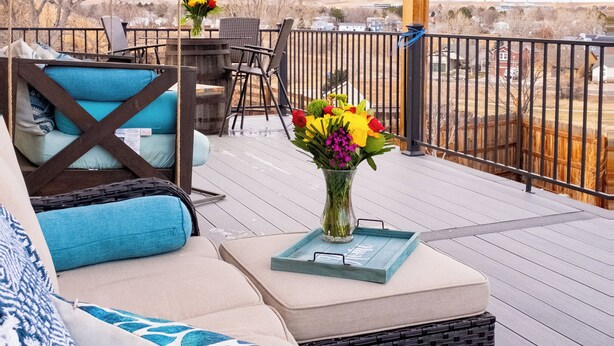 Un espacio al aire libre techado con terraza de madera, una mesa, sillas y una lámpara colgante.