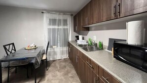 Una cocina compacta con armarios de madera oscura, encimera de granito, microondas negro y una zona de comedor con mesa y sillas.