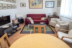 A living room with a red sofa, a wooden coffee table, a TV, and a dining table with chairs.