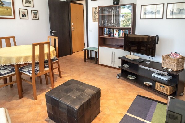 A living room with a dining table, chairs, a television, a bookshelf, and a small table.