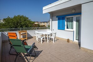 A balcony with a table and chairs, a small wooden stool, and two lounge chairs.