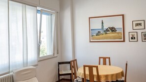 Una habitación con una mesa de comedor, sillas, un ventanal con cortinas y un cuadro en la pared.