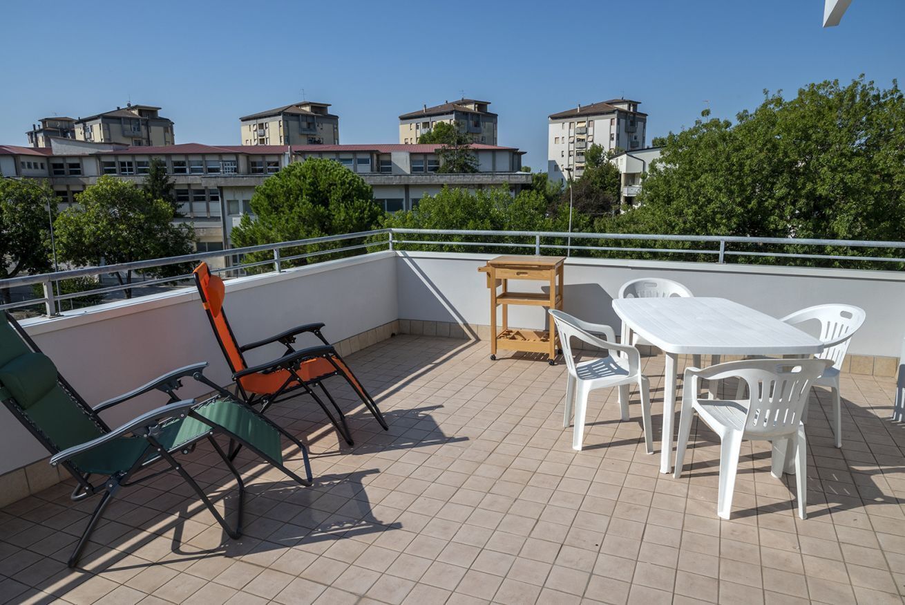 A rooftop terrace with a table and chairs, a wooden bench, and a railing.