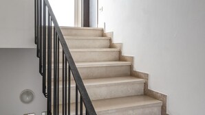 Una escalera con peldaños color crema y barandillas negras que lleva a una habitación con pared blanca y ventana.