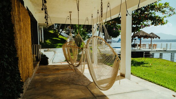 A covered outdoor seating area with wicker chairs and a view of the water. - Bendito Teques (Jojutla)
