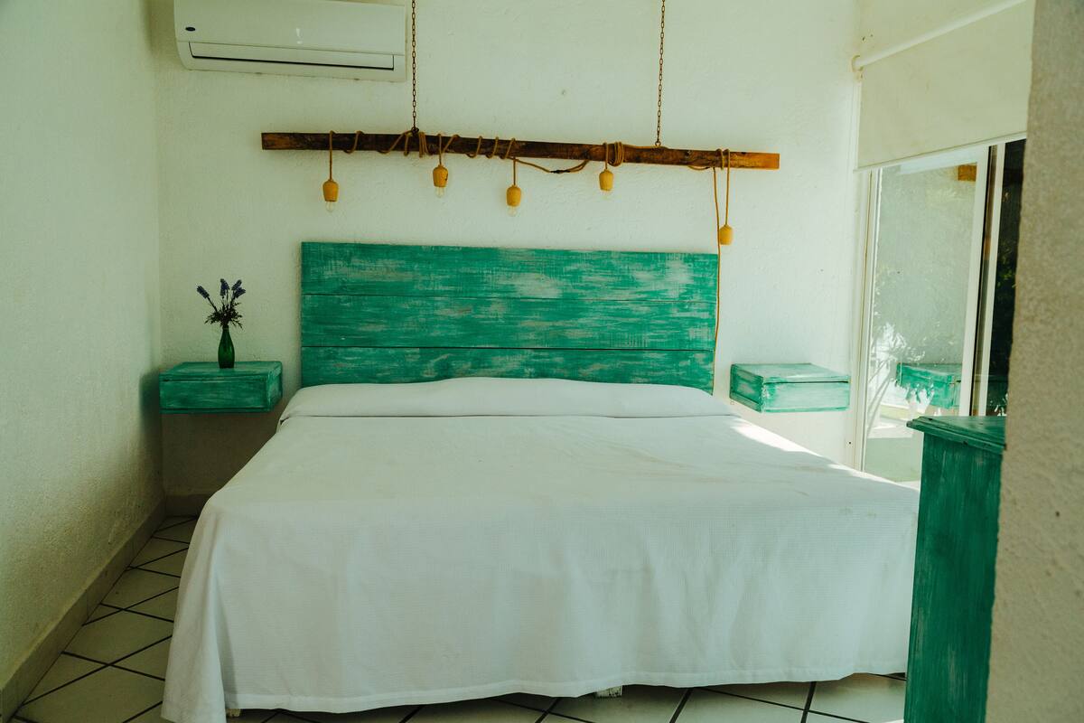 A bedroom with a bed, a nightstand, a small table with a vase, and a window.