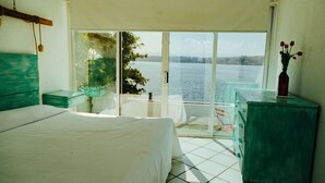 A bedroom with a large bed, a green dresser, and a view of a body of water through a glass door. - Bendito Teques (Jojutla)