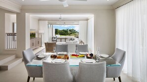 Un comedor moderno con una mesa de vidrio, sillas tapizadas en gris y un ventilador de techo.