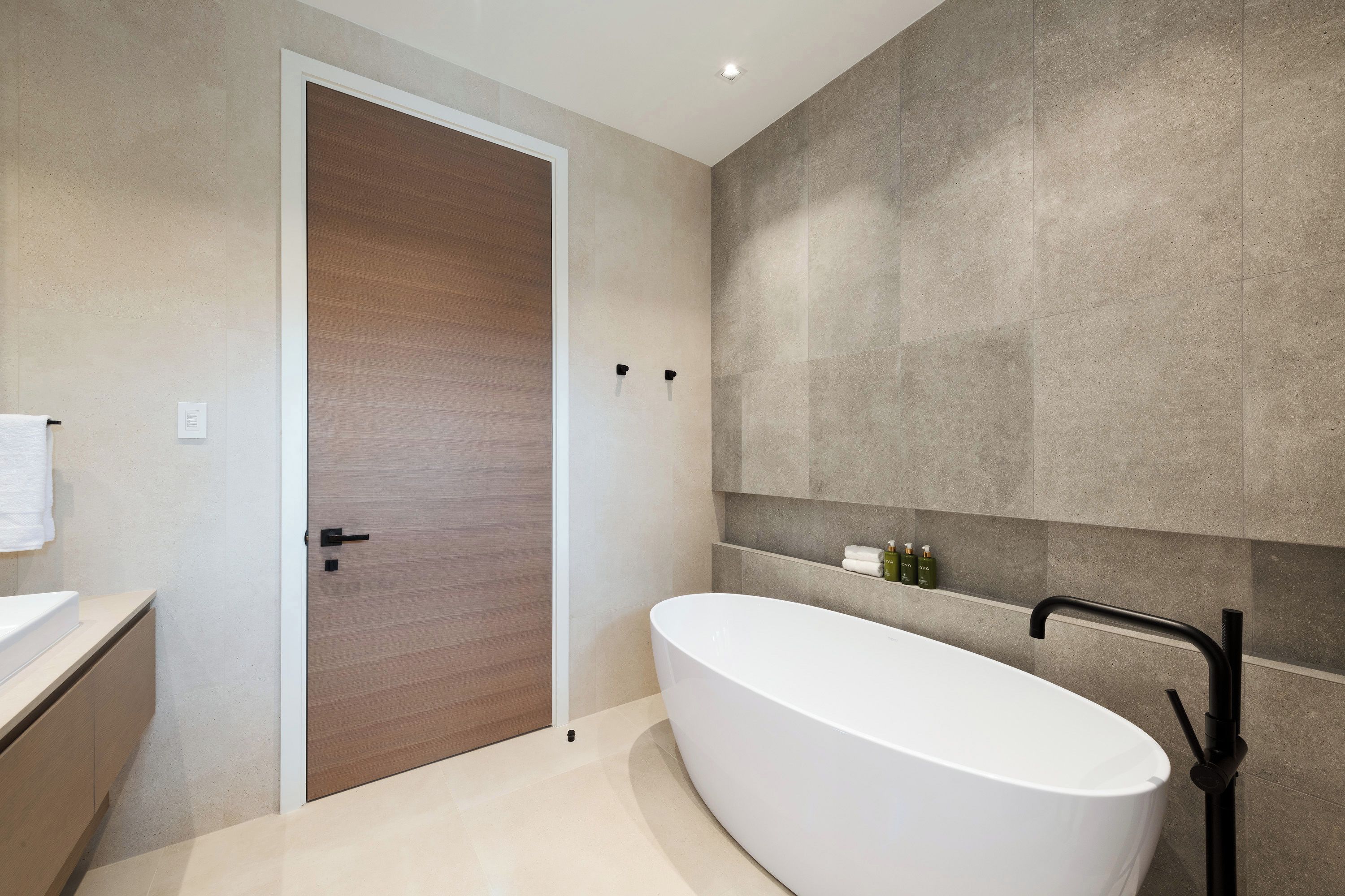A modern bathroom with a freestanding bathtub, a wooden door, and a wall-mounted shelf with toiletries.