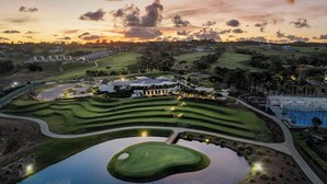 Ein Golfplatz mit Teich, Gebäuden und einem Sonnenuntergangshimmel.