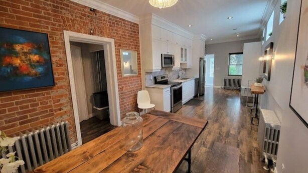 A modern kitchen with white cabinets, a stainless steel refrigerator, and a wooden dining table. - Family Friendly Century Home - 3 Bedrooms, 2 Baths (Toronto)