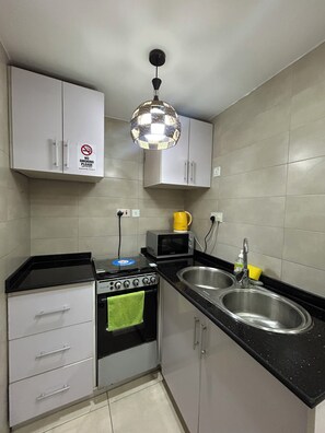 A kitchen with a stove, microwave, sink, and cabinets. - Hillside Gardens (Lagos)