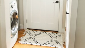 A laundry room with a white door, a washing machine, and a rug on the floor. - Serenity in South Wedge: desirable walking community meets vibrant tranquillity! (Rochester)